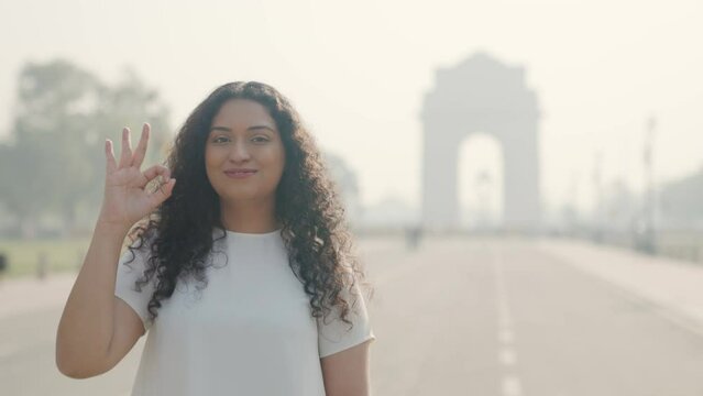 Happy Indian Girl with Curly Hair Doing Ok Sign at India Gate