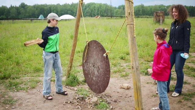 Mother and two children play with big metal gong outdoor at summer