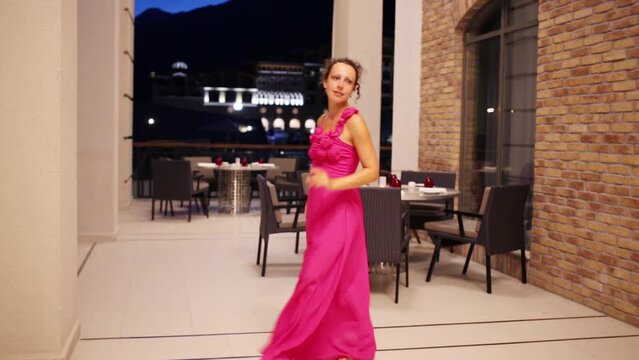 Beautiful woman in pink dress dances at summer cafe at evening