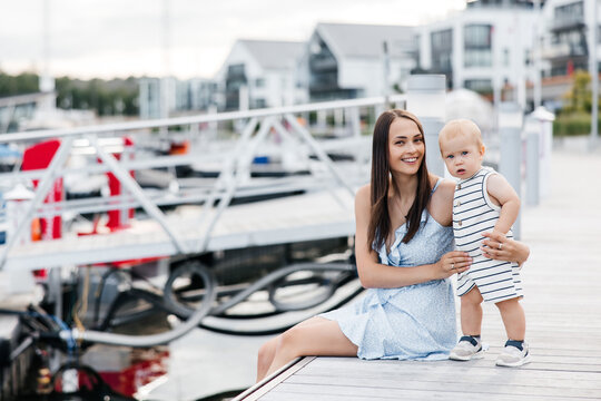 Portrait of a young happy mother and her little son. Happy young mother and her cute son dressed in summer clothes and walking on a wooden pier. Happy motherhood and childhood