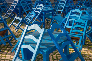 Empty blue wooden tables and chairs outside a cafe or restaurant, stacked.