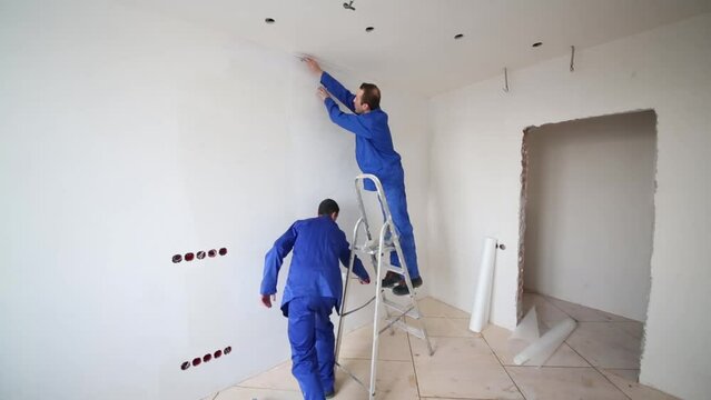 Man cuts excess fiberglass, next man smears glue on the wall