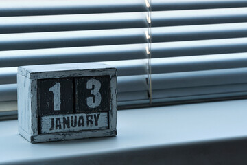 Morning January 13 on wooden calendar standing on window with blinds.