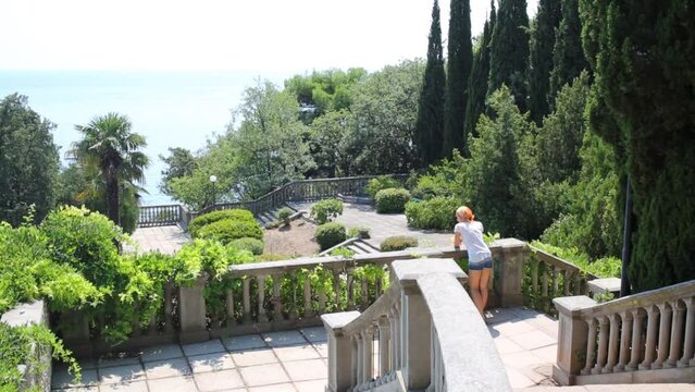 Woman on staircase looks at sea in tropical garden