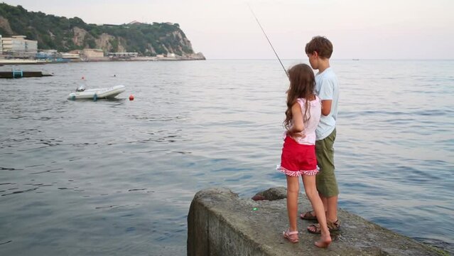 Boy and girl fishing in sea. Boat floats out of focus