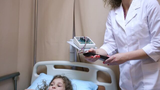 Health worker with remote control and little girl lying on bed 