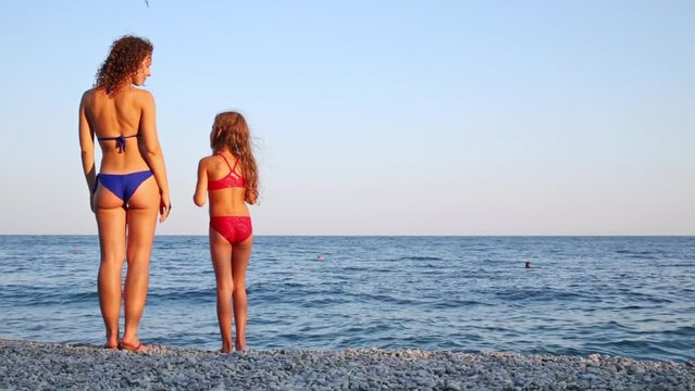 Young mother with daughter in the swimsuit standing on a beach
