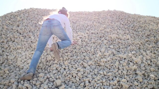 Back of girl in jeans crawling on gravel pile at sunny day