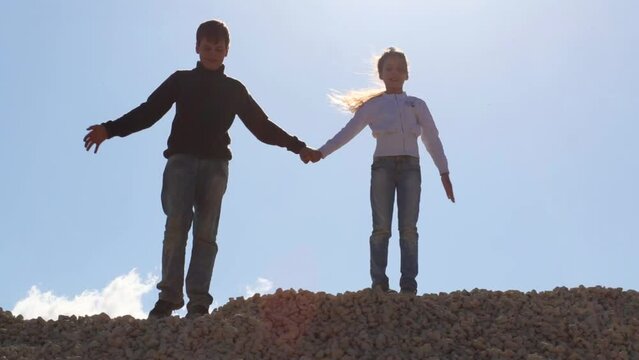 Girl and boy stand on stone pile and hold hands at sunny day