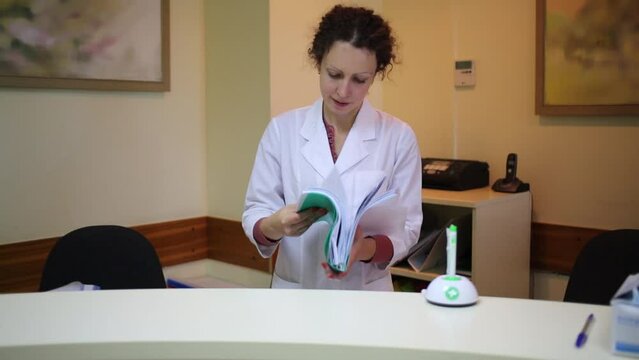 Female doctor in lab coat looks through folder with documents.