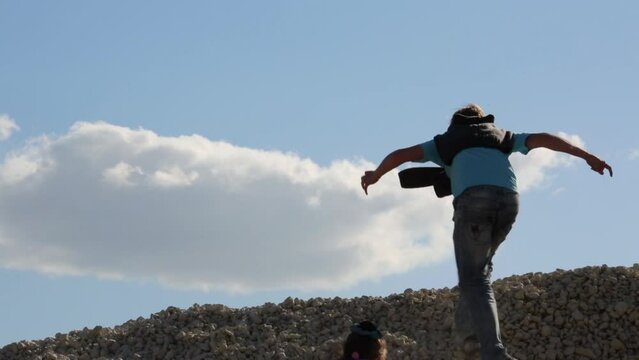 Boy and girl in jeans climb on gravel pile and descend 