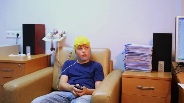 doctor looks at display with live charts, boy in special cap sits