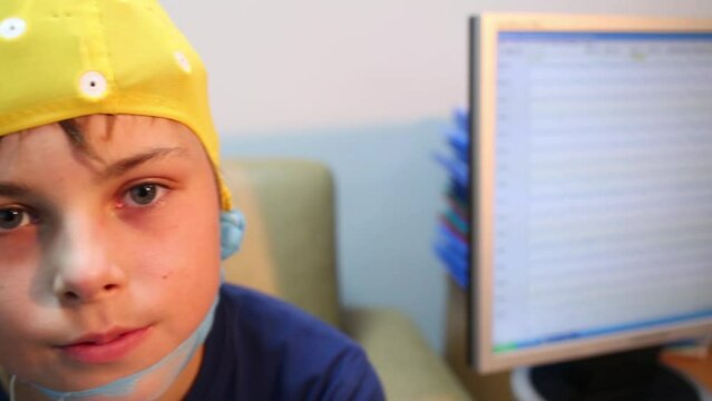 Boy in cap for electroencephalography sits near monitor 