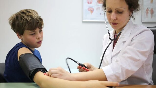 Female doctor pumps up tonometer cuff at boy shoulder.
