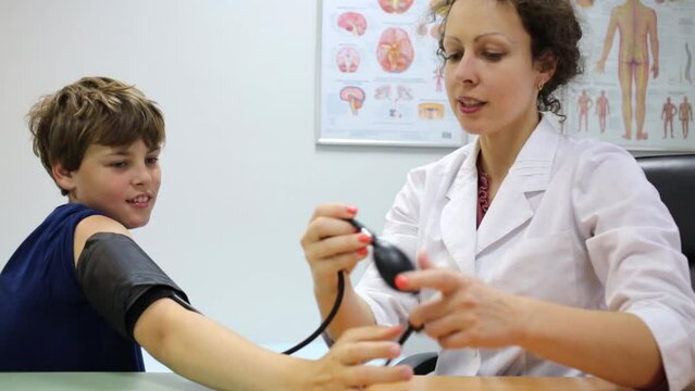Female doctor puts on tonometer cuff onto boy shoulder.