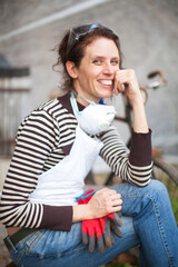 Cheerful Adult Woman Smiling for a Portrait in a Break from Renovation Work of an Old Men's Bicycle from the 1920s in the Background