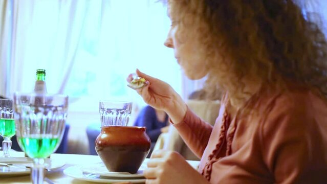 Curly woman eats from ceramic pot sitting at table in cafe.