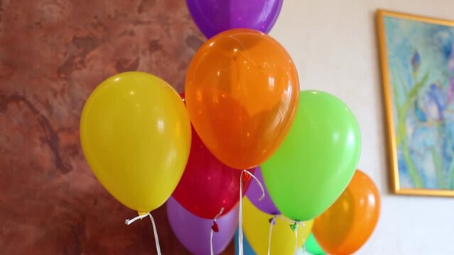 Colored helium balloons in room near wall with picture