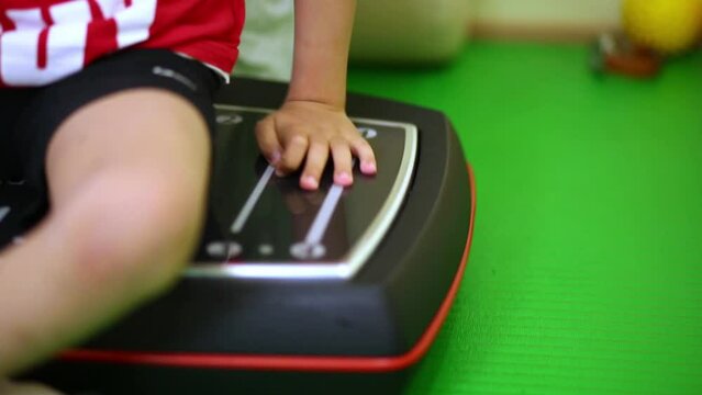 Little boy sits on working vibrating platform in medical center.
