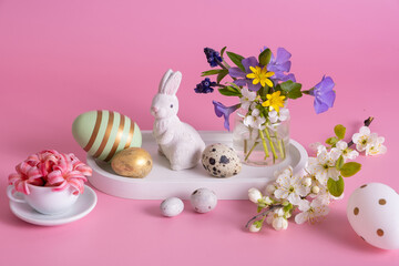 White rabbit, flowers and Easter eggs on a pink background. Easter hunt concept.