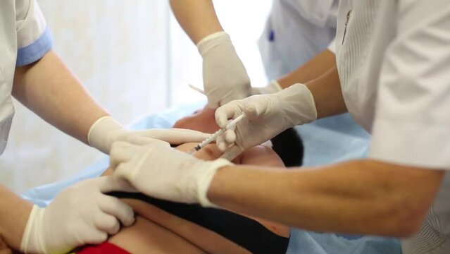 Group of doctors injections boy arm on medical table.
