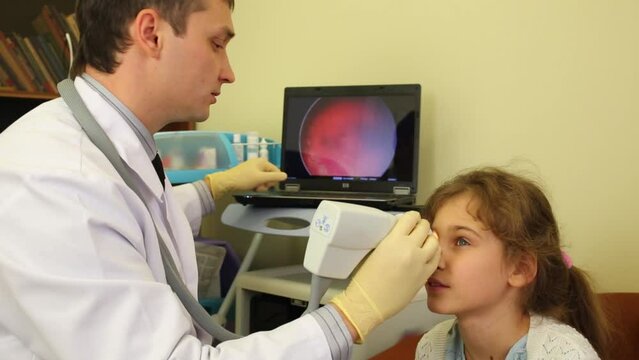 Ophthalmologist inspects girl eye and points at laptop screen