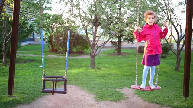 Happy girl in skirt on swing on children playground at summer