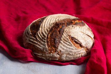 Freshly baked banneton sour dough bread on red linen cloth on a white wooden table