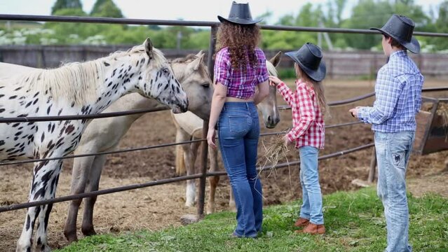 Cowgirl and two children stand at fence of paddock with horses.