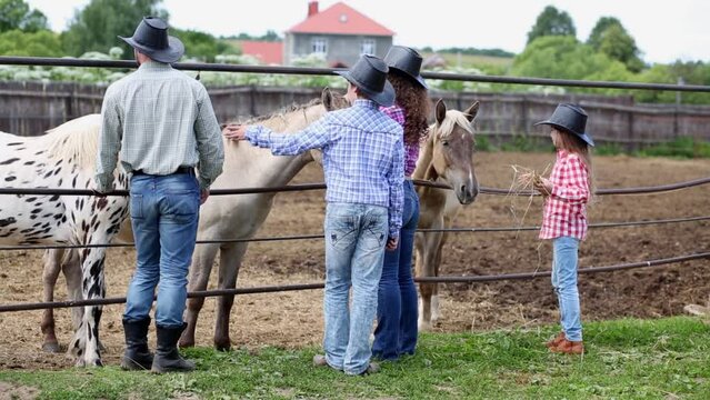 Cowboy family stands at metal fence of paddock with horses.