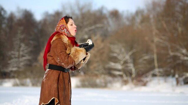 Young woman stands holding bird on bright winter day.
