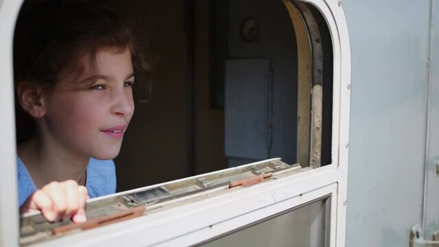 Little girl looks ou in the window of train car and waves farewell
