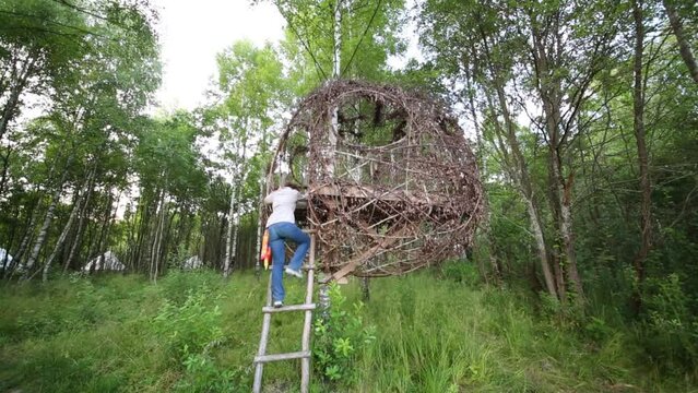 Woman climbs into round twig house on tree among forest