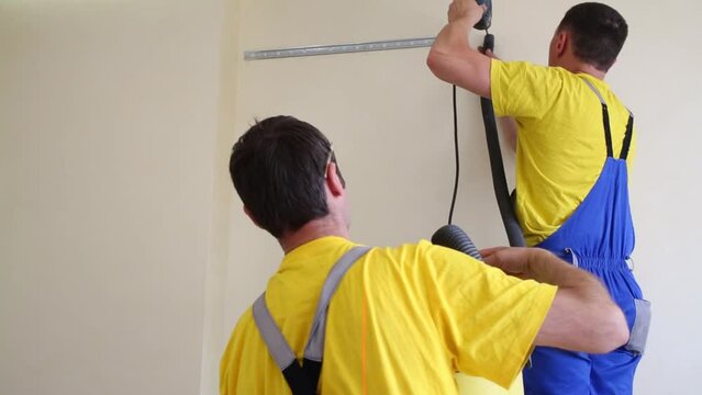 Workers drills hole in wall and collect dust with vacuum cleaner