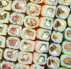 Close-up of a lot of sushi rolls with different fillings lie on a wooden surface. Macro shot of...