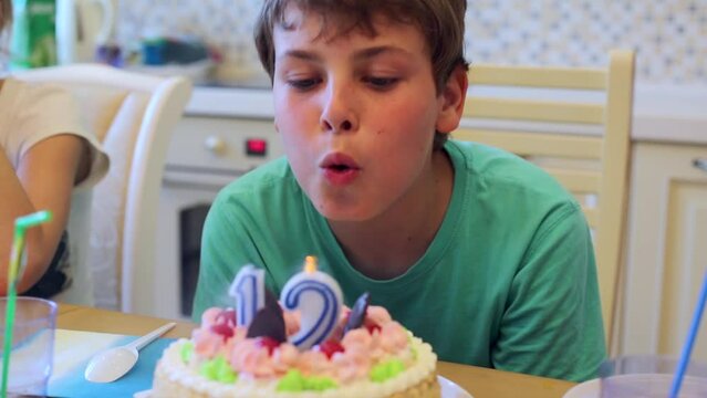 Boy sits at table with birthday cake blows up burning candles.