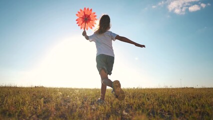 kid run pinwheel. little baby girl silhouette play with windmill toy wind in the park. happy family...