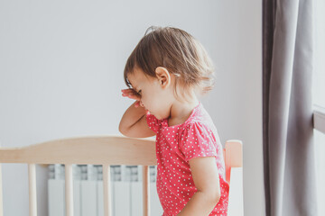 one little baby stands in his crib and rubs his eyes, wants to sleep, profile view © Evgeniia Primavera