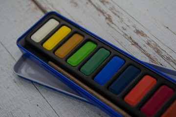 set of watercolor paints in cuvettes in close-up. The artist's accessories on a wooden table.