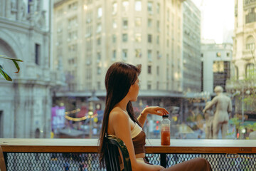 young Latin woman looks through a window of an establishment with a juice the city. copy space