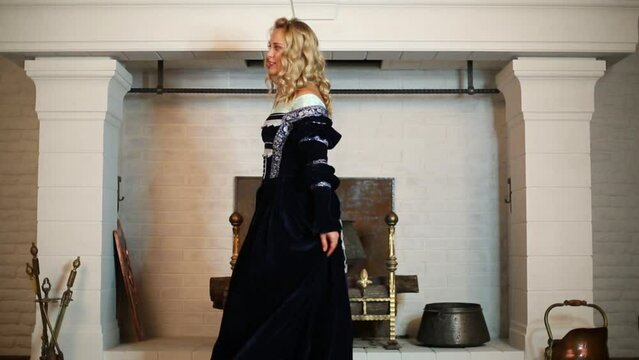 Blonde woman in medieval costume dances near fireplace
