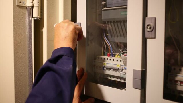 hand closes small glass door of heat consumption meters in wall