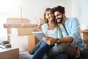 Smiling couple making online purchase using digital tablet in new apartment. Young couple,...