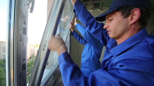 Two workers set window to new installed window-frame.