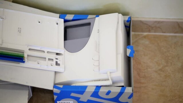 Home intercom in open cardboard packaging box on the floor.