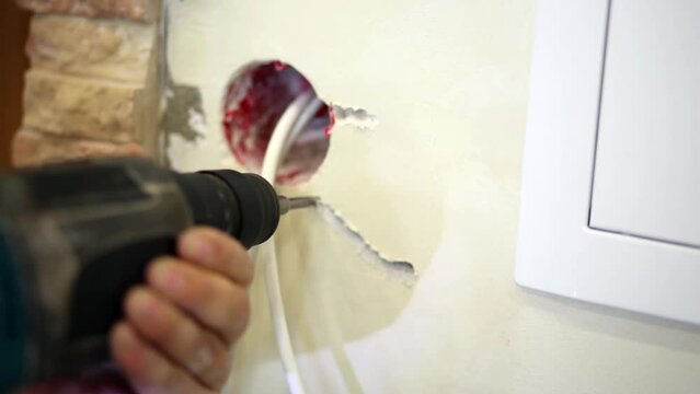 Worker makes trench for cables in plaster using drill.