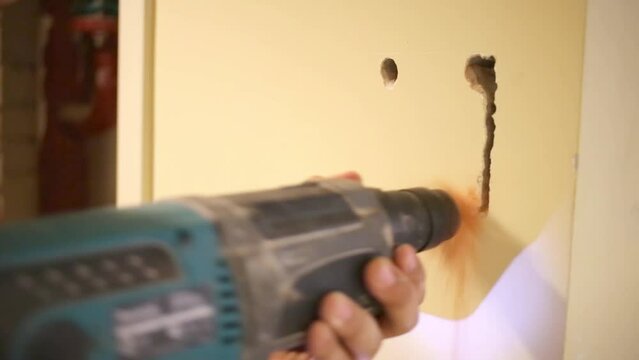 Worker makes trench in plaster on wall using drill.