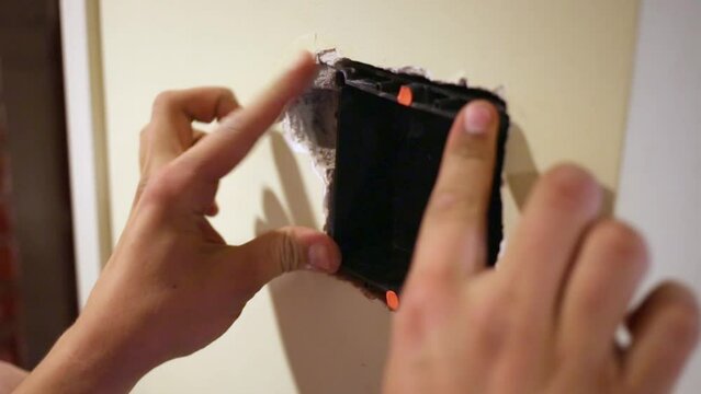 Worker hands insert mounting box into the hollow in wall.