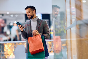 Young happy man using app on smart phone while shopping at mall.
