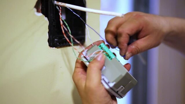 Worker hands connect wires to terminal block of electronic device